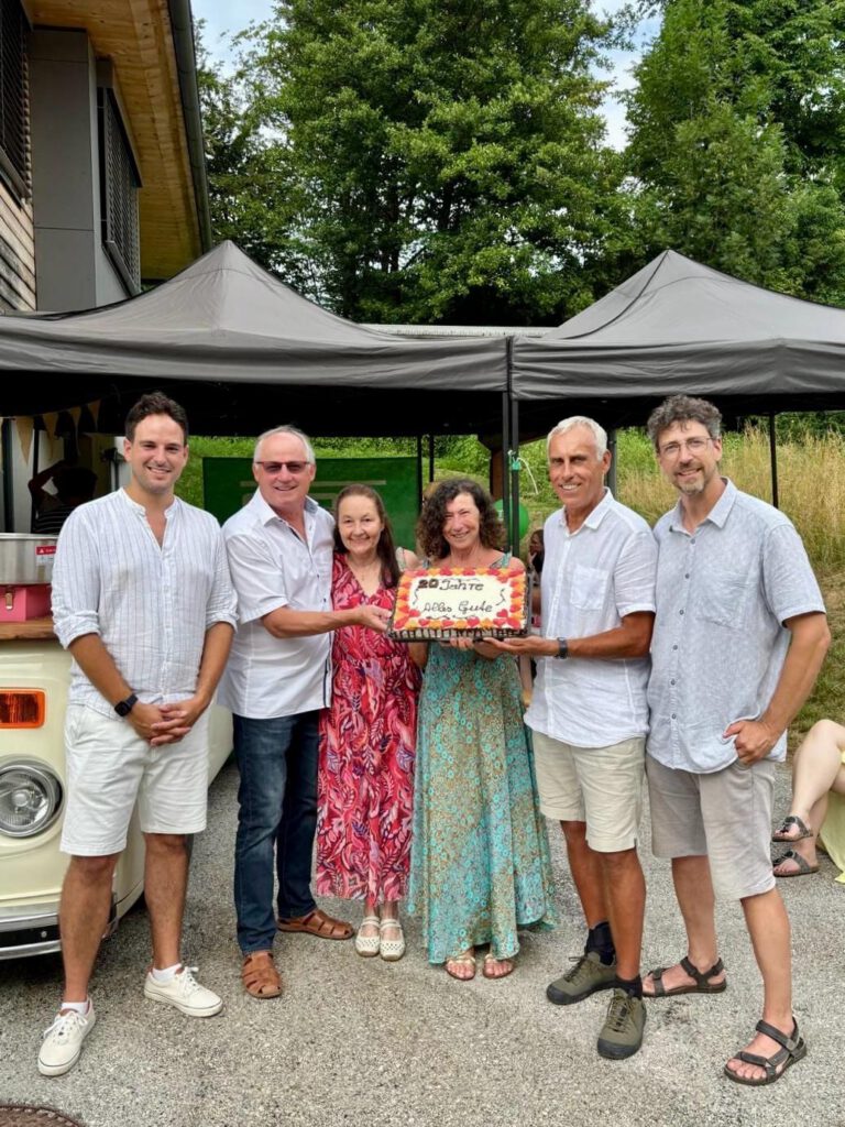Sechs Personen, darunter SOT-Gründer:innen und Teammitglieder, halten gemeinsam eine Torte mit der Aufschrift „20 Jahre – Alles Gute“ beim Sommerfest 2025 vor dem Firmensitz.
