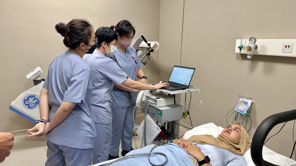 Healthcare professionals in blue scrubs perform a vascular measurement with the AngE™ system from SOT Medical Systems on a patient lying in a hospital bed.